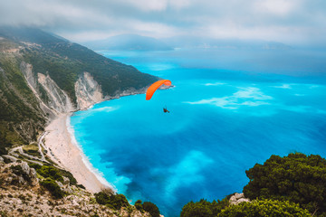 Aerial view of the paraglider flying over gorgeous Myrtos beach. Amazing water colors and beautiful...