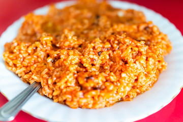 Closeup of fresh vibrant red tomato sauce paella fried hot pepper rice chili on plate in sauce, plain greasy shiny grains in restaurant on white plate