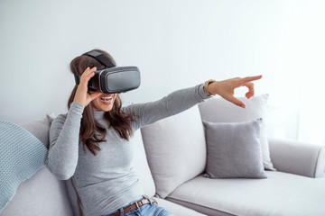 Smiling young woman using VR headset at home on couch