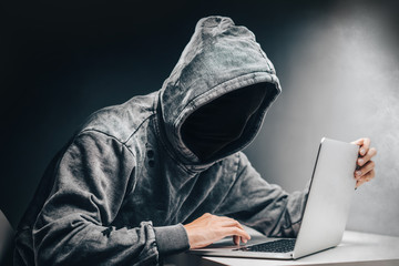 Cyber crime. Male hooded hacker with hidden face accessing to personal information on a computer in...