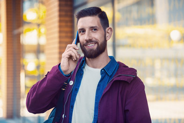 Young man wearing winter clothes with a smartphone in his hand, walking in the street. Sun flare