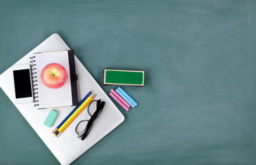 Back to school concept with technology and stationery on a green chalkboard background
