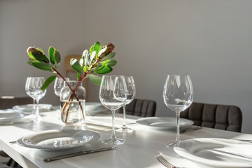 Long table with many glasses and plates and green flowers in vase