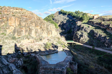 A landscape of the Aragonese countryside hills, with a stone water tank, bare trees and green...