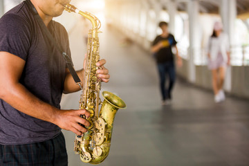 A street musician plays the saxophone with blurry people