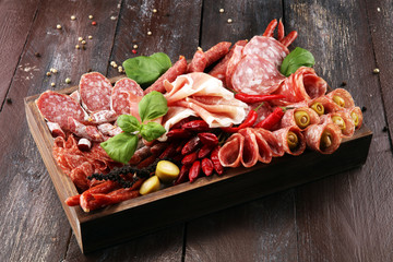 Food tray with delicious salami, pieces of sliced prosciutto crudo, sausage and basil. Meat platter with selection