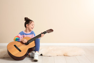 Cute little girl playing guitar on floor in room. Space for text