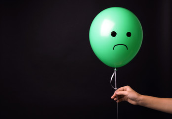 Woman holding balloon with sad face on black background, space for text. Threat of depression