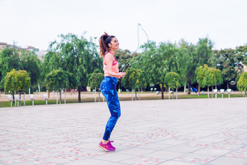 Fit beautiful woman with jumping rope in a park. Fitness female doing skipping workout outdoors on a sunny day.