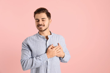 Portrait of young man holding hands near heart on color background. Space for text