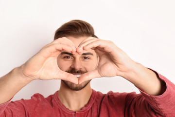 Man looking through heart made with his hands on white background