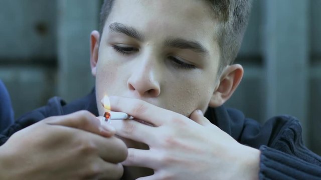 Teenager lighting cigarette to classmate, peers pressure, youth bad habits