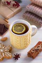 Knitted yellow cup with tea drink, cookies, cinnamon, winter decorations. Warm and cozy atmosphere while cold season