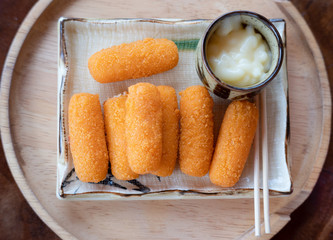 Cheese sticks served with sauce on wooden plate.