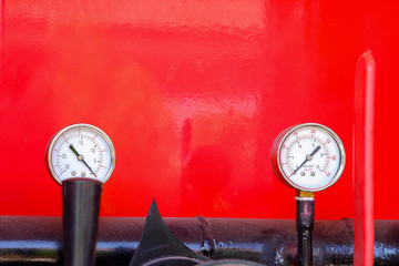 Water pressure gauge in the pipeline on red background.
