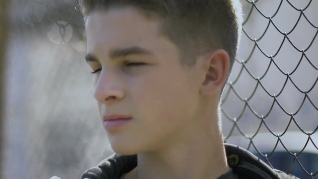 Teenage boy leaning on iron fence, thinking about his future, juvenile colony