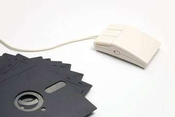 Retro white three-button computer mouse with five-inch floppy disks for storing information on a...