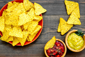 Snack for party. Mexican nachos near salsa and guacamole sause on dark wooden background top view