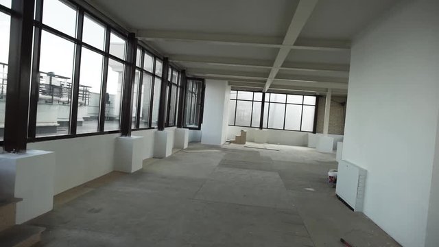 Large empty apartment with big black framed windows, grey floor and white walls and ceiling without any furniture and people in daylight.