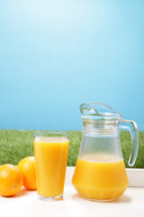 Two fresh oranges, a glass and a jar full of orange juice