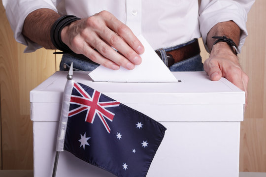 An Australian citizen inserting a ballot into a ballot box. Australia flag in front of it