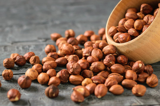Hazelnut kernels are poured from a wooden bowl onto a dark wooden table.