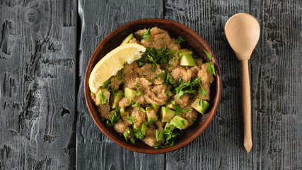 Clay bowl with amaranth seed salad with avocado, lemon and parsley on a dark wooden table. The view from the top.