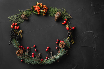 Crown of Christmas tree branches, pine cones, berries, nuts, on black stone background. Xmas and Happy New Year theme. Flat lay, top view