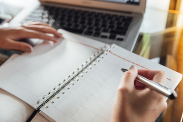 Young business woman in casual dress sitting at table in cafe and writing in calendar notebook....