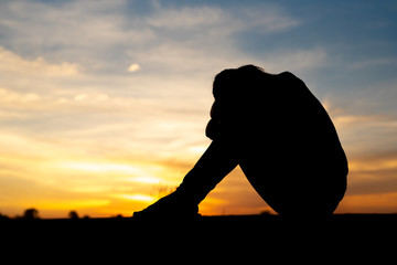 Silhouette of sad and depressed women sitting at walkway of park with sunset