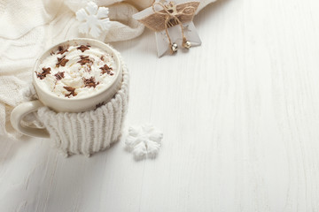 A cup of hot winter drink with whipped cream and a dusting powder with an asterisk, white snowflakes and knitted scarf on a wooden table. Christmas concept in bright colors. Copy space.