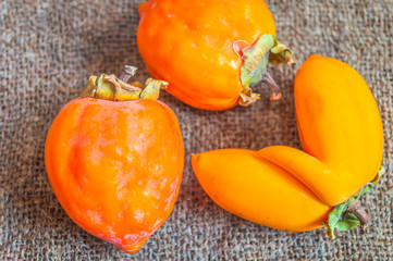 Close up top view of orange Persimmons fruit kept on a jute mat. One fruit has a unique shape
