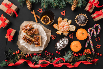 Christmas composition of fir branches, pine cones, berries, gifts and red slack, on black stone background. Candies, sweets, mandarins, gifts and tea. Xmas and Happy New Year theme. Flat lay, top view