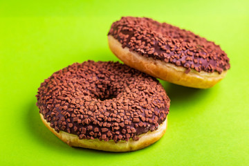 Two delicious chocolate donuts with sprinkle on bright green background