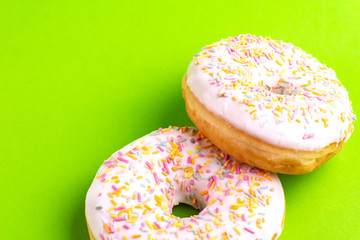 Two delicious vanilla donuts with sprinkle on bright green background