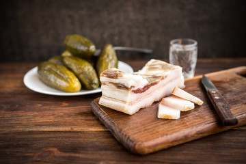 Traditional Ukrainian and Russian appetizer when dining. Food when drinking alcohol. Vodka and salt pork fat and pickled cucumbers on dark wooden