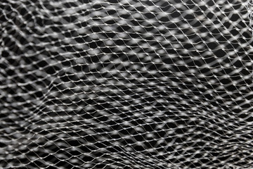 Abstract black and white mesh texture with selective focus. Light lines and dark background. Wavy, scaly pattern.
