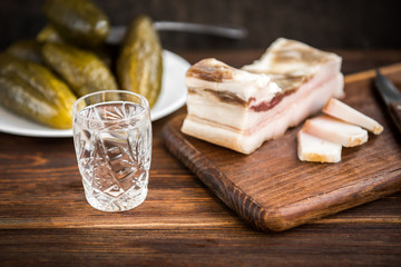 Traditional Ukrainian and Russian appetizer when dining. Food when drinking alcohol. Vodka and salt pork fat and pickled cucumbers on dark wooden