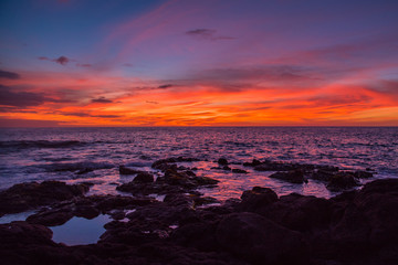 Orange sunset over lava rock and the ocean