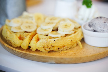 closeup of waffle with sliced banana and ice cream on wood tray