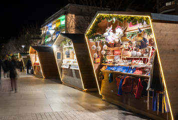Wide shot of a Christmas market booth in Merano south tyrol italy, with a beautiful light during night and people bassing by on the street, christmas feeling