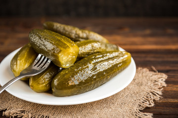 Pickled cucumbers on white plate on wooden rustic background