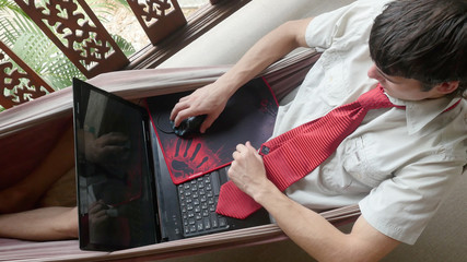 Young man using laptop computer, resting in a hammock