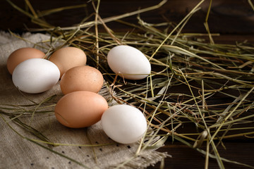 white and brown eggs on straw and wooden dark background.