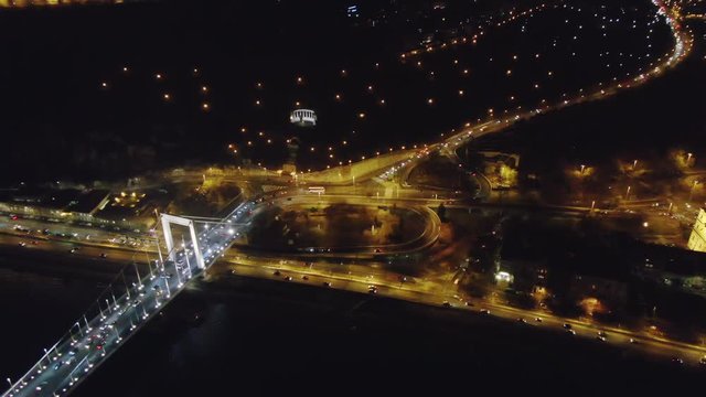 Aerial shot of glowing Budapest with bright bridge across dark river in night time, Hungary