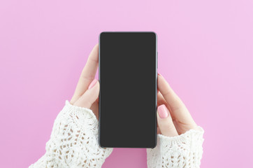 Woman hands holding mobile phone on pink background with copy space. Flat lay. Top view. Smartphone mock up