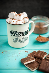 A cup of coffee with marshmallow, a knitted blue scarf, chocolate bar and cocoa on green wooden background. Drinks and sweets.
