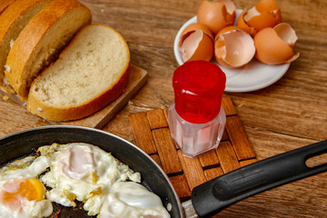 Fried egg on in a frying pan with bread on kitchen board.