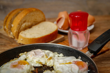 Fried egg on in a frying pan with bread on kitchen board.