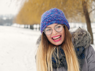 Beautiful happy girl in the cold in a blue hat and round glasses.